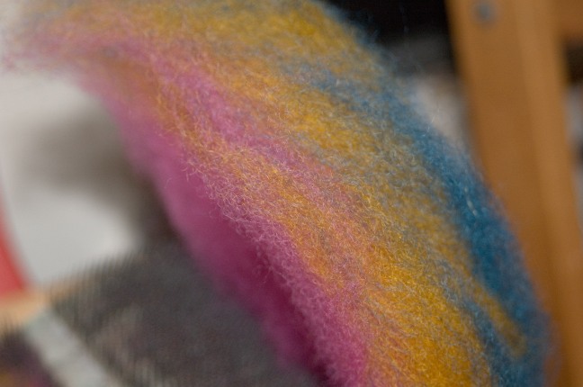 magenta yellow and blue layers of wool on a drum carder